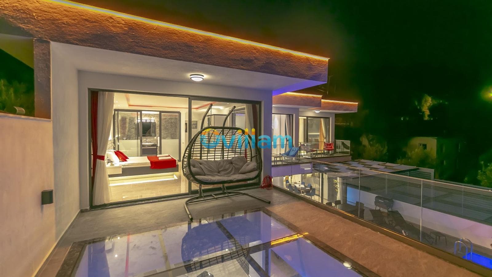 Geceleri aydınlatılmış balkonda asma salıncak bulunan modern villanın dış görünümü.