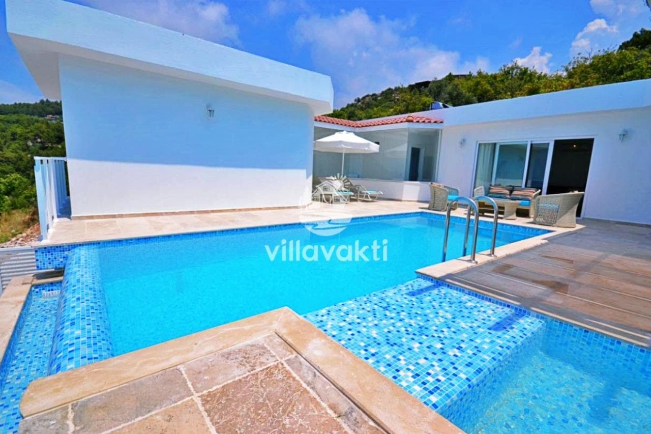 Açık renk taş terasta yer alan yüzme havuzu ve arka planda villa dış cephesi.