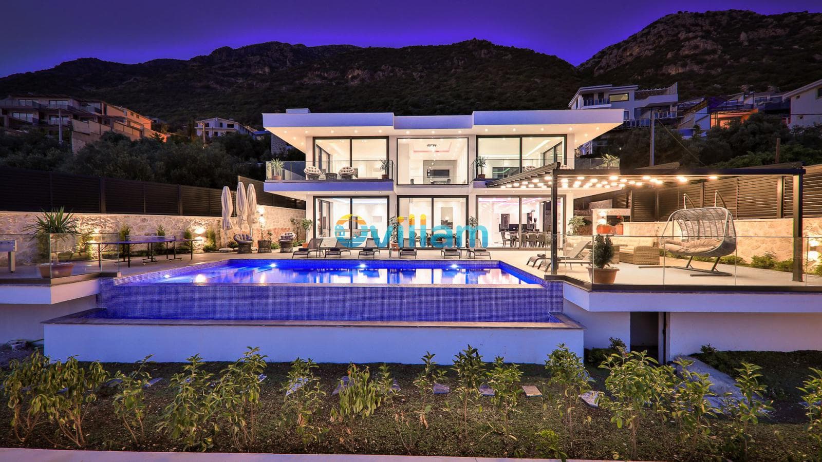 Akşam aydınlatmalı modern iki katlı villanın havuz ve bahçe görünümü.