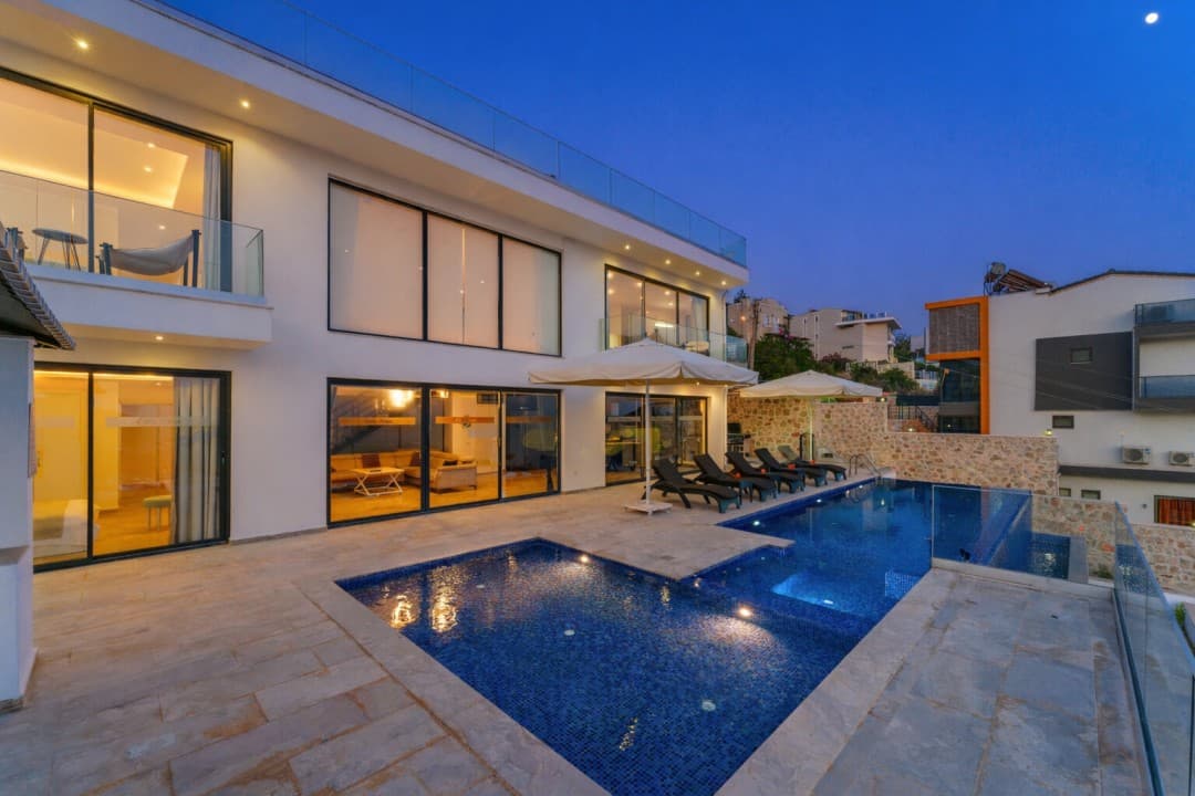 Akşam saatlerinde aydınlatılmış havuz ve iki katlı modern villa dış cephesi.