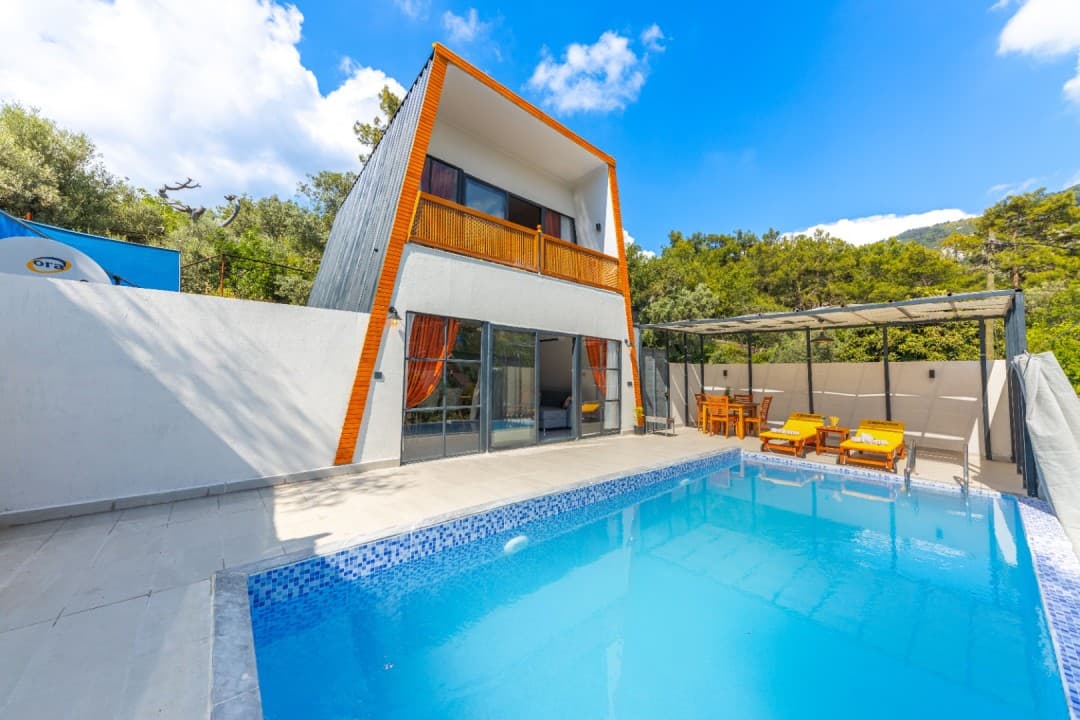 Önünde yüzme havuzu, şezlonglar ve yemek masası bulunan, ahşap detaylı iki katlı modern villa.