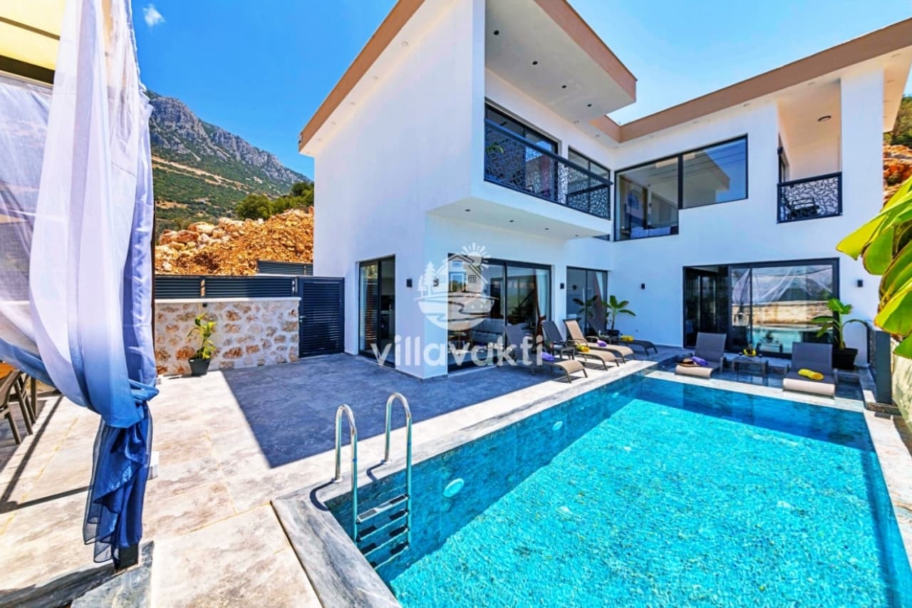 Dağ manzaralı havuz kenarında şezlonglar bulunan beyaz iki katlı lüks villa.