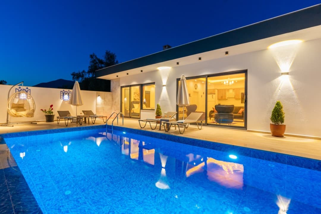 Aydınlatmalı havuz kenarında şezlonglar ve salıncak bulunan villa dış cephesi