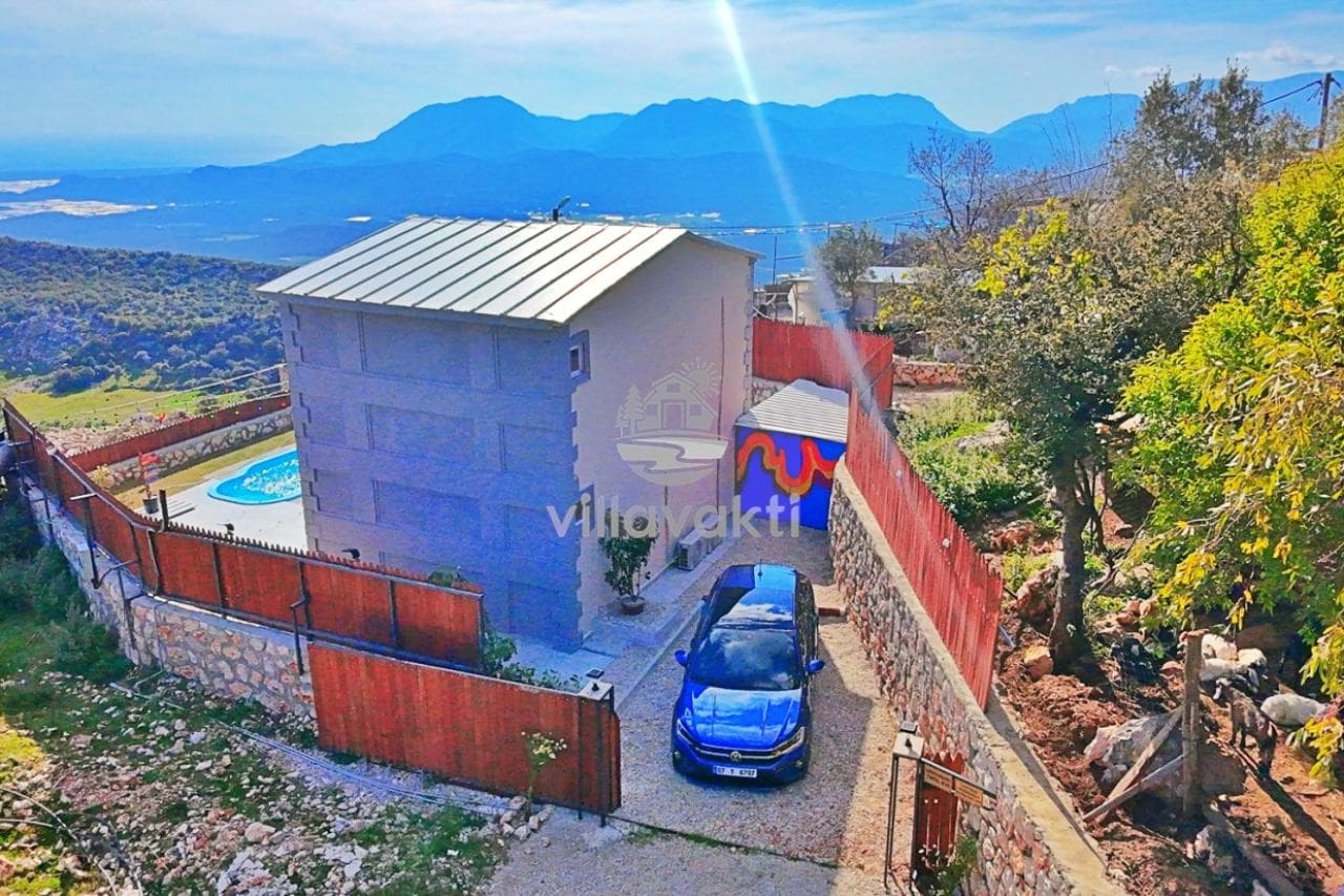 Dağlar ve doğa manzaralı tepede yer alan, önünde park etmiş mavi otomobil olan villa.