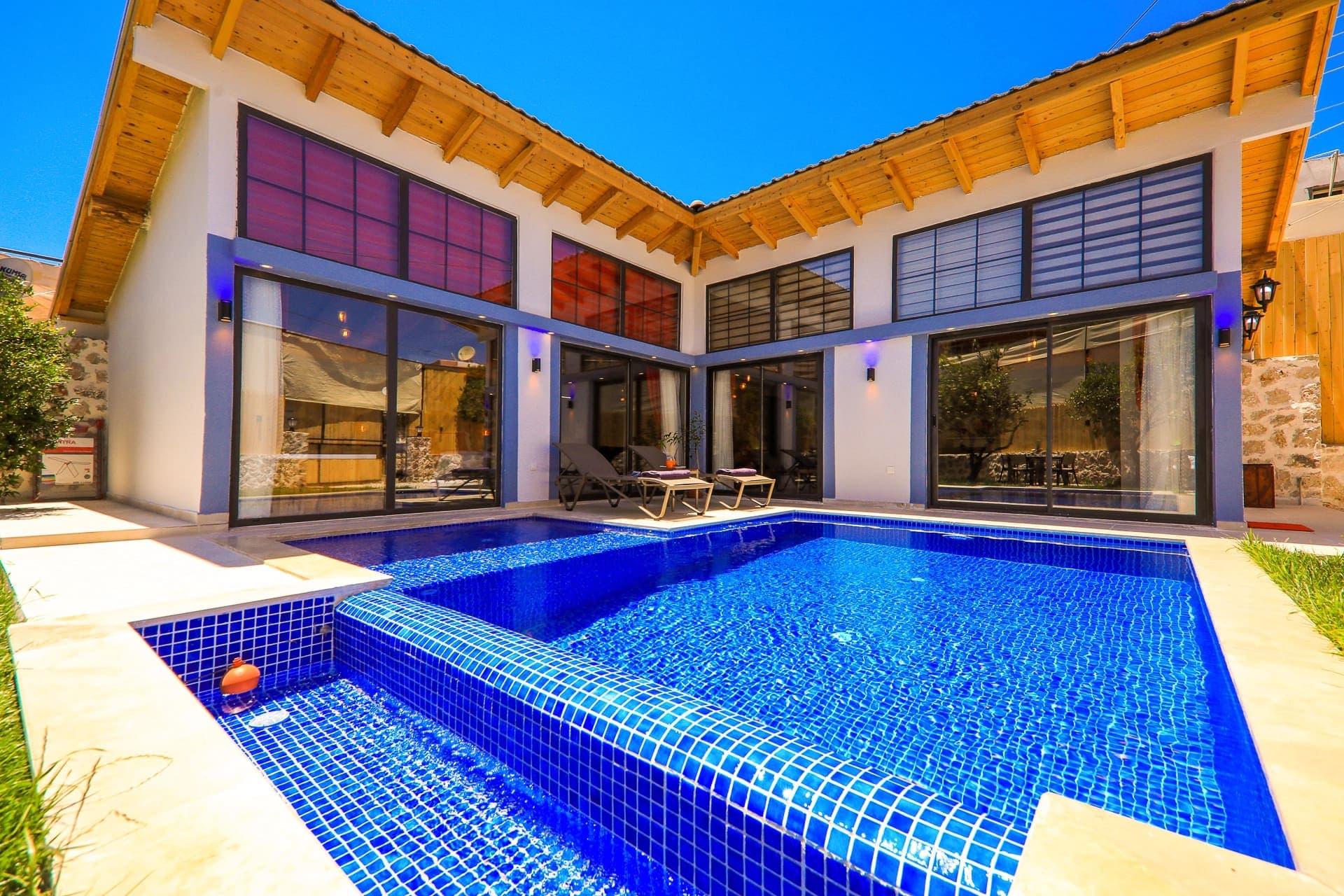 Açık mavi havuzlu ve ahşap detaylı modern villanın dış cephesi.