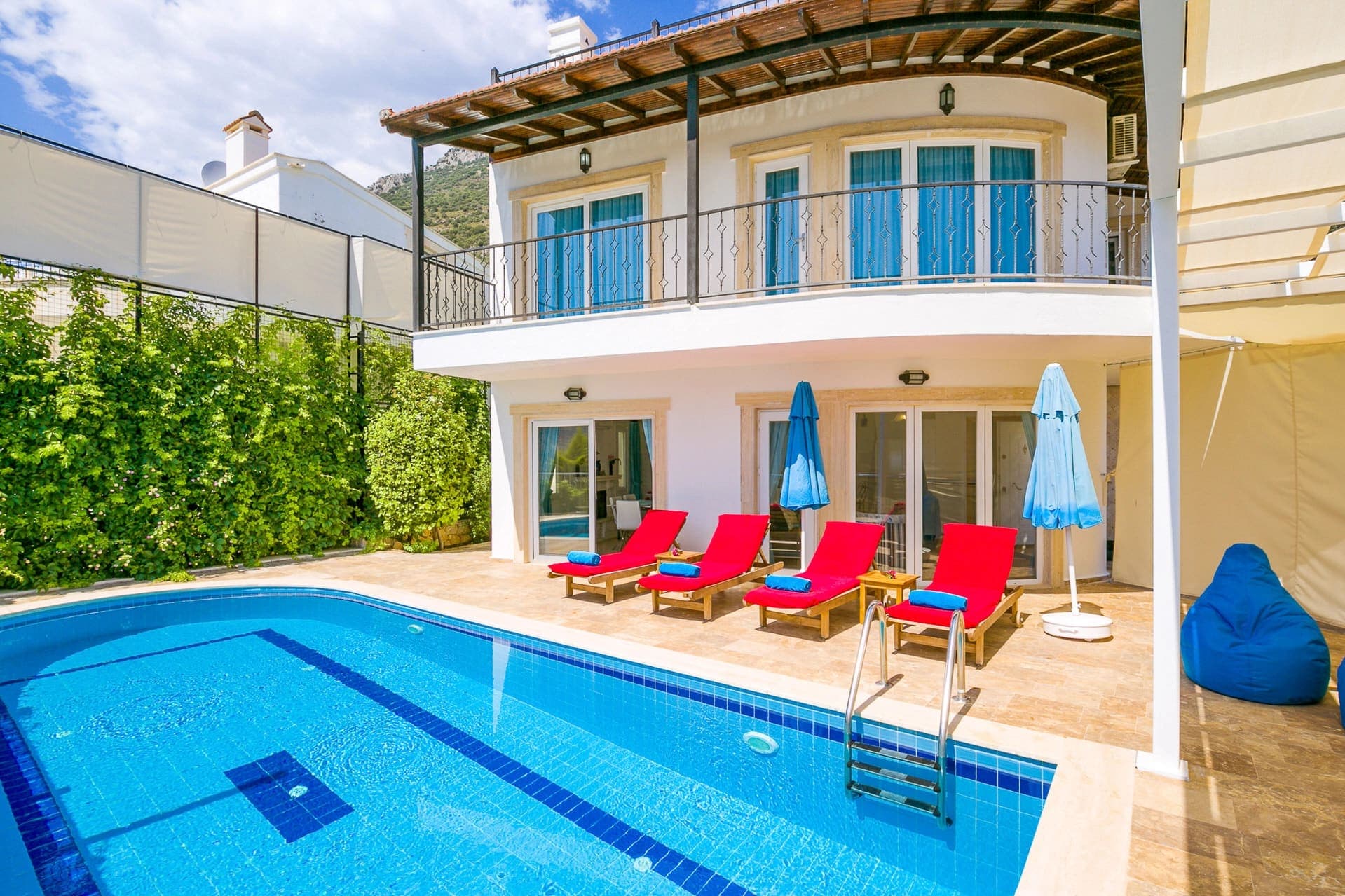 Bahçesinde havuz ve kırmızı şezlonglar bulunan iki katlı beyaz villa.