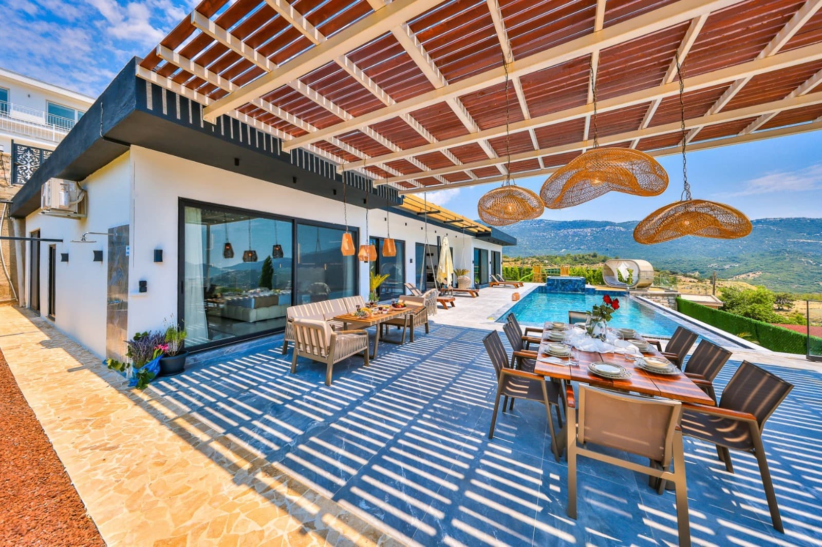 Geniş terasta havuz, oturma grubu, yemek masası ve ahşap pergola gölgeliği bulunuyor.