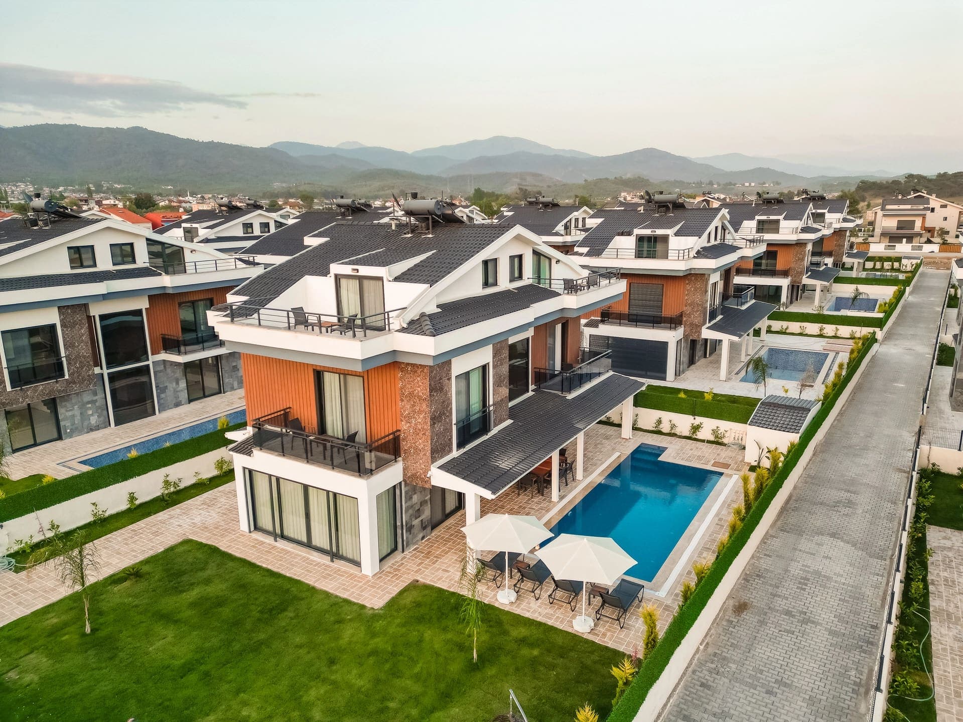 Havuzlu modern villaların yer aldığı site görünümü ve uzakta dağlar.