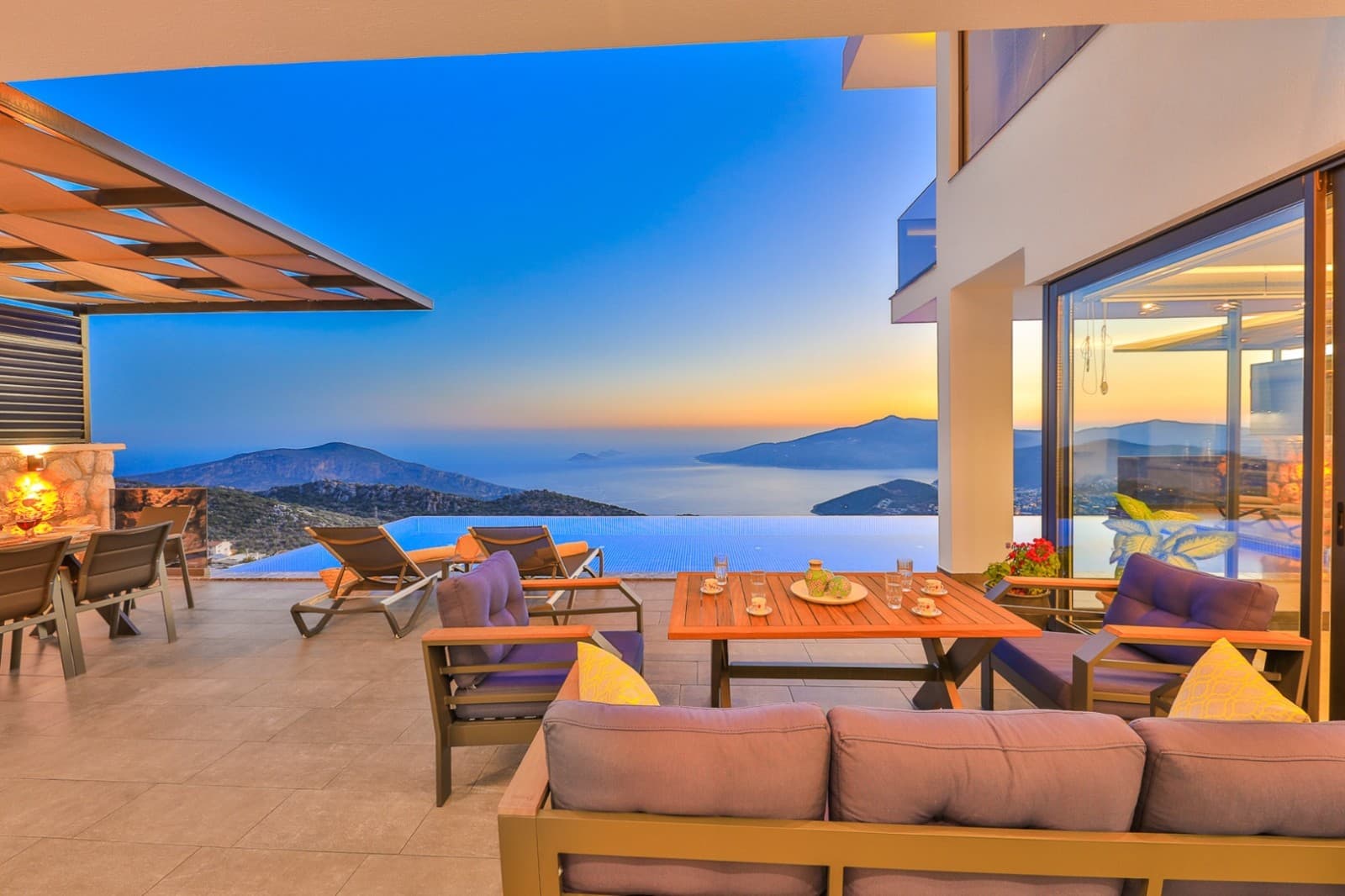 Gün batımında deniz ve dağ manzaralı, açık teraslı ve havuzlu villa.