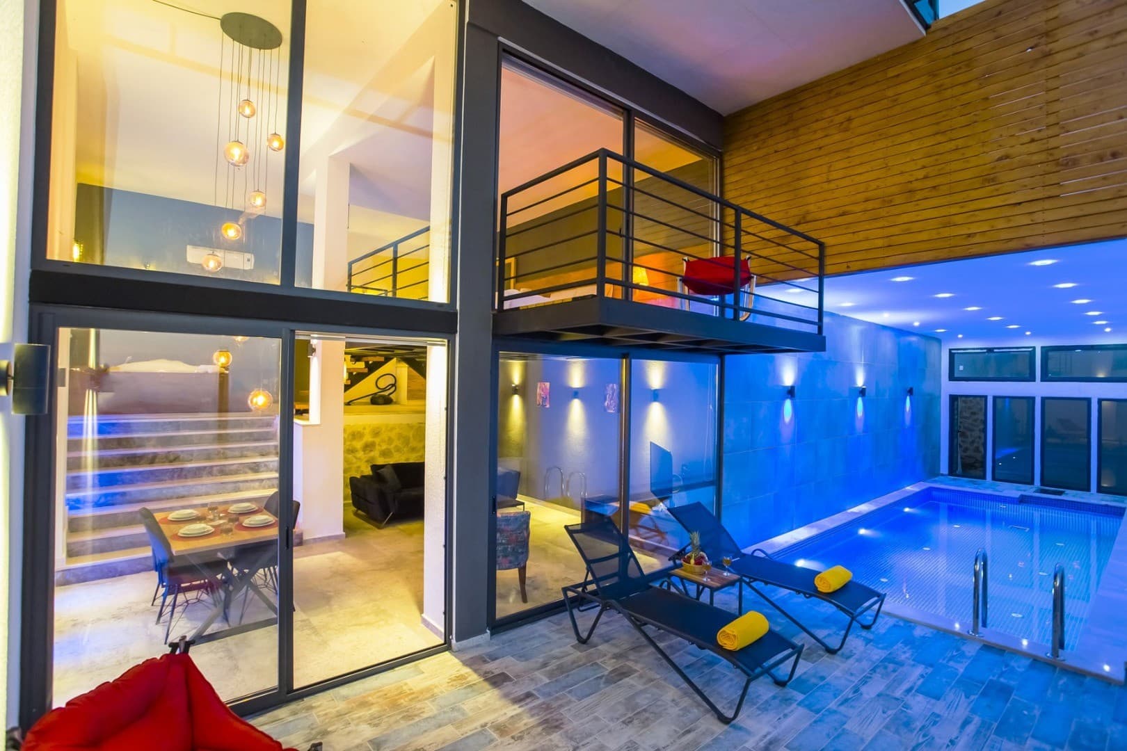 İç mekanda kapalı havuz, şezlonglar, yemek masası ve asma kat bulunan modern tasarımlı villa.