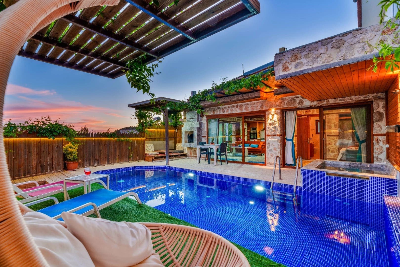 Ahşap detaylı taş villa önünde havuz, şezlonglar ve oturma alanı.