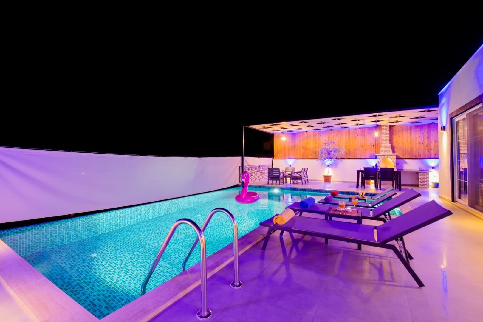 Gece aydınlatmalı, şezlonglu ve flamingo deniz yatağı bulunan özel havuzlu villa terası.