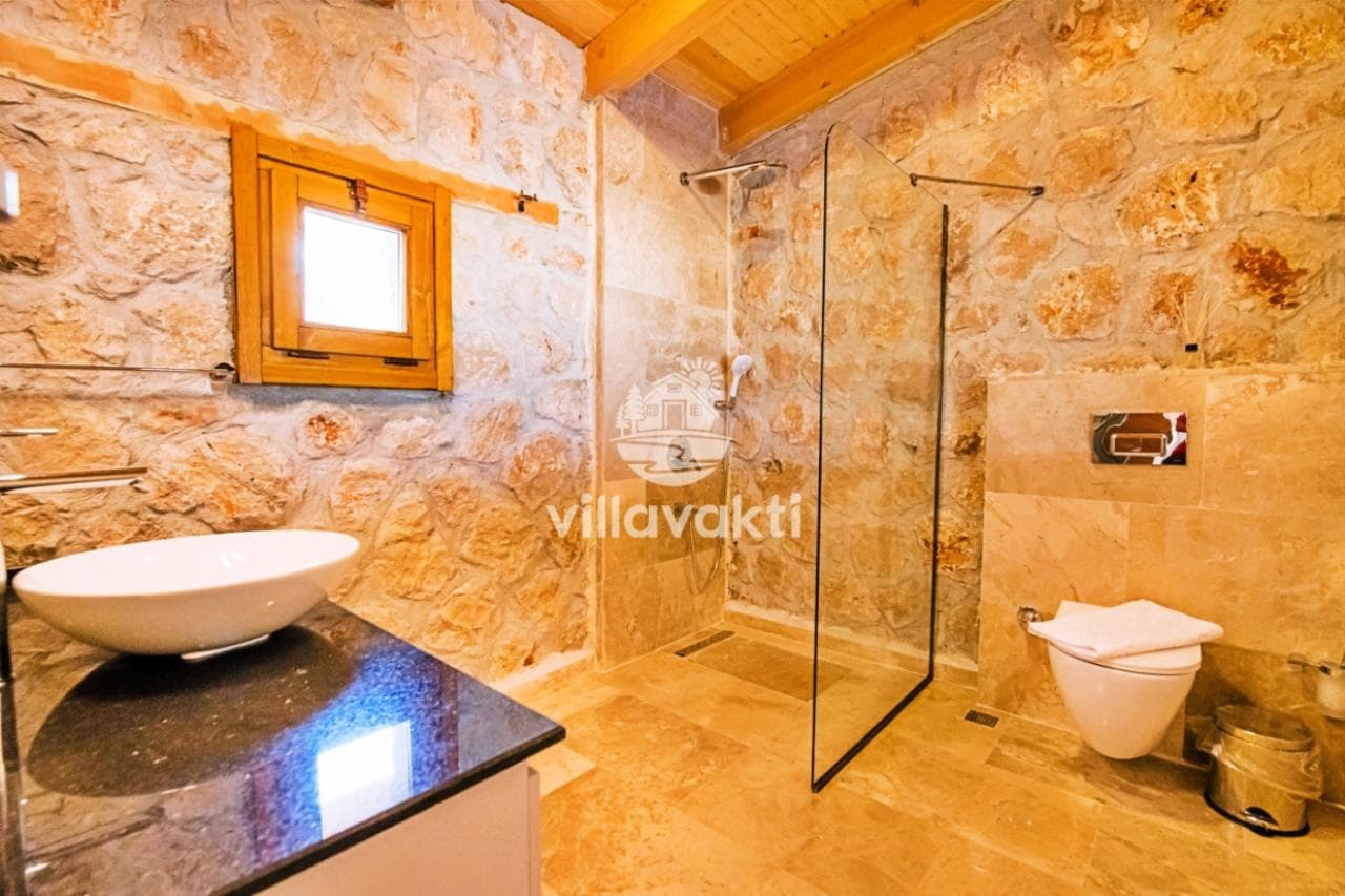 Taş duvarlı banyoda duş kabini, lavabo ve klozet bulunmaktadır.