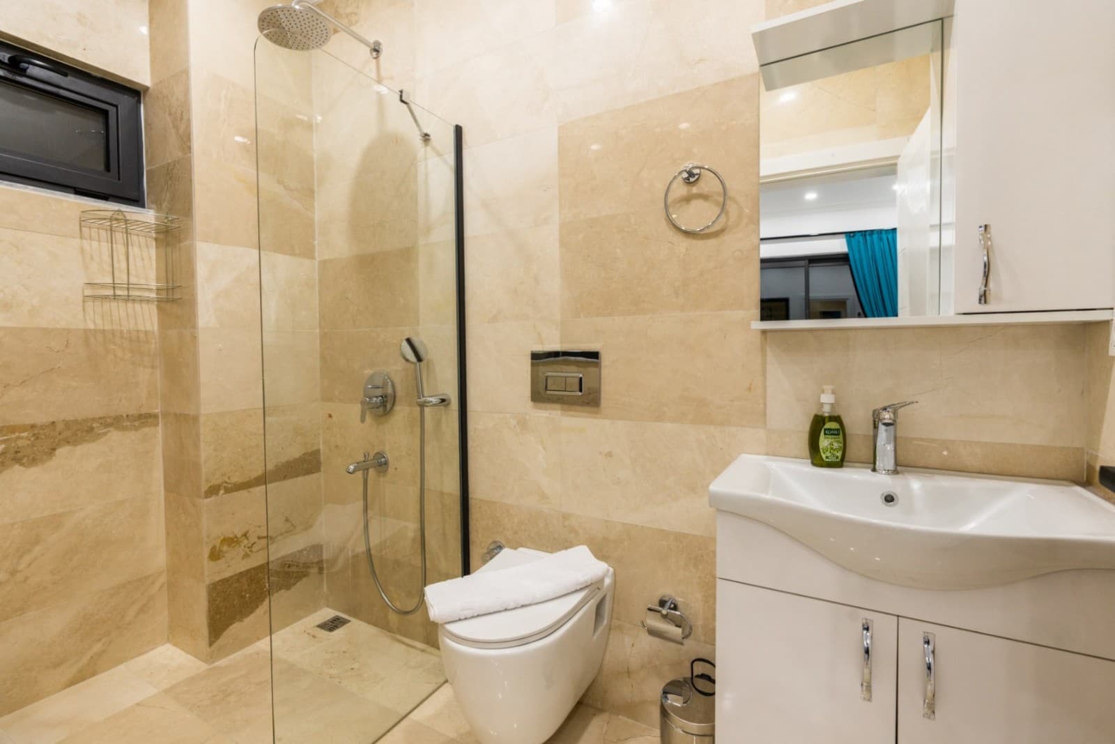 Bej seramik kaplı duş alanı, klozet ve lavabo bulunan banyo.