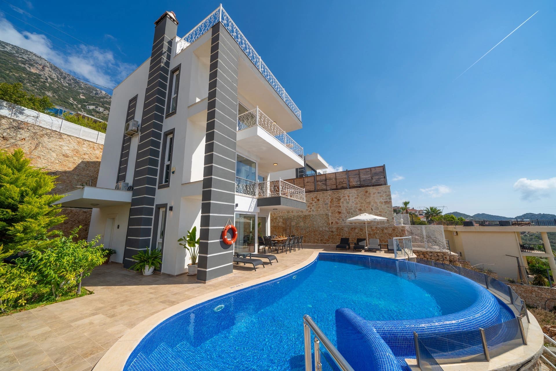 Önünde yüzme havuzu ve şezlonglar bulunan çok katlı villa dış cephesi.
