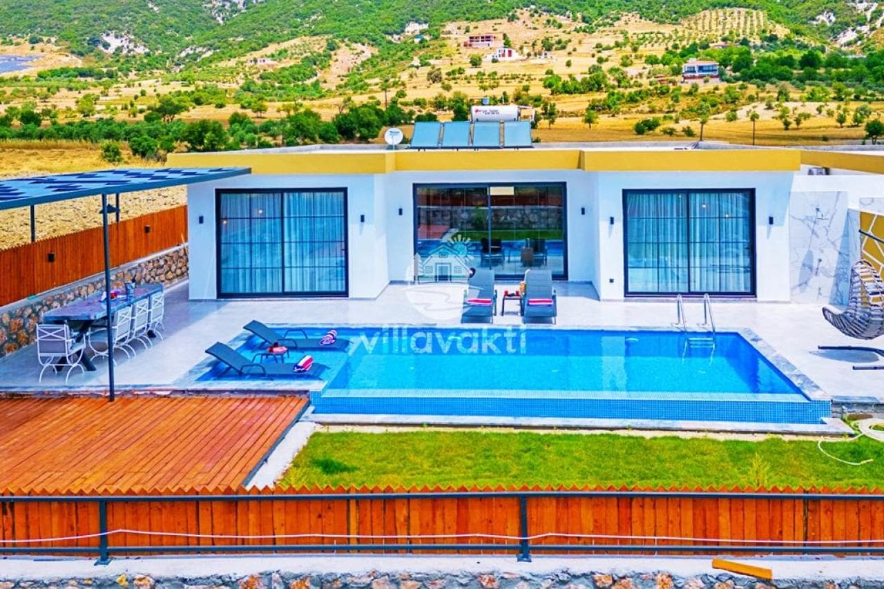 Tek katlı beyaz villanın önünde yüzme havuzu, şezlonglar ve doğa manzarası var.