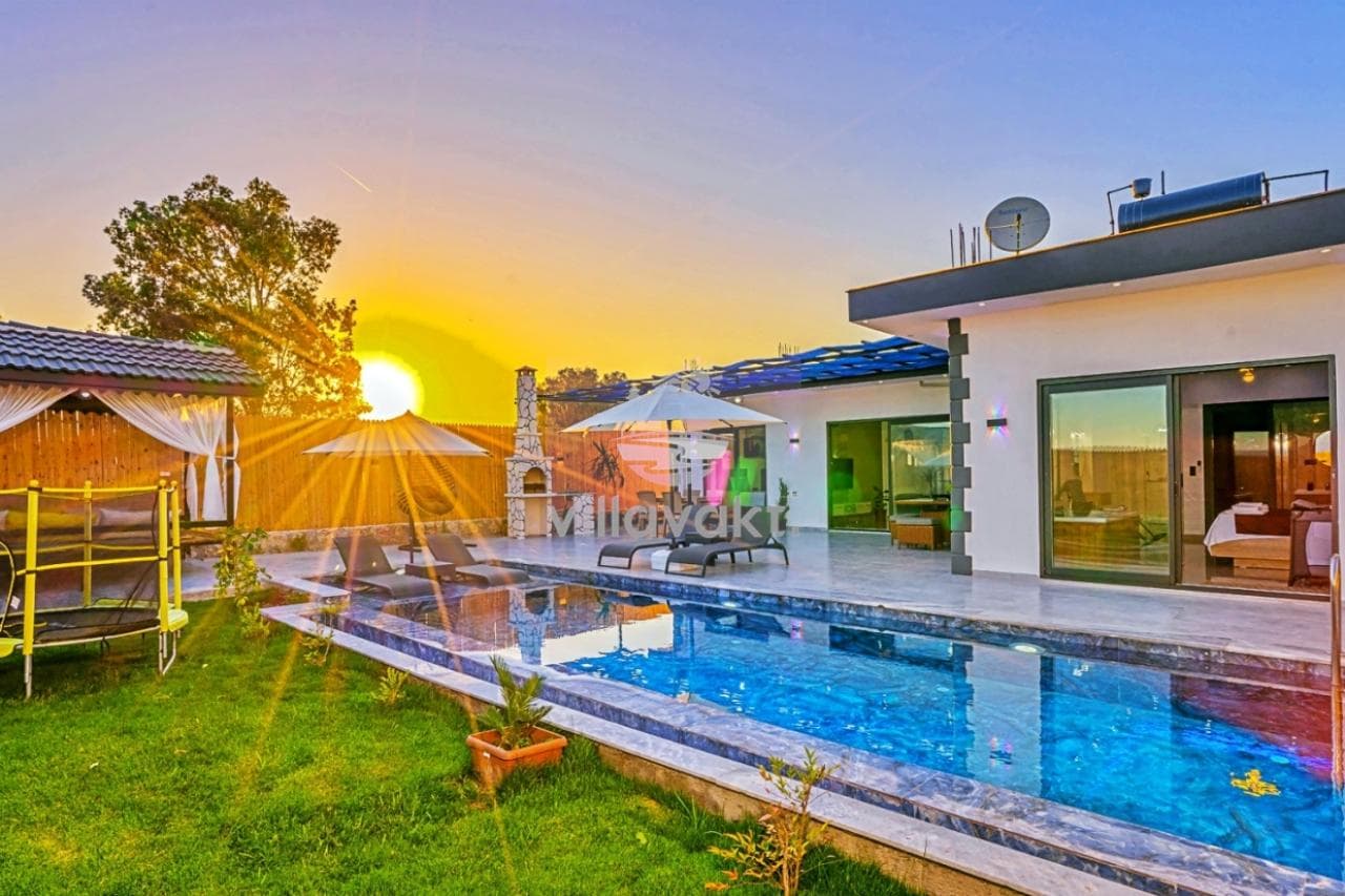 Gün batımında havuz başı, şezlonglar, çardak ve trambolin bulunan villa bahçesi.