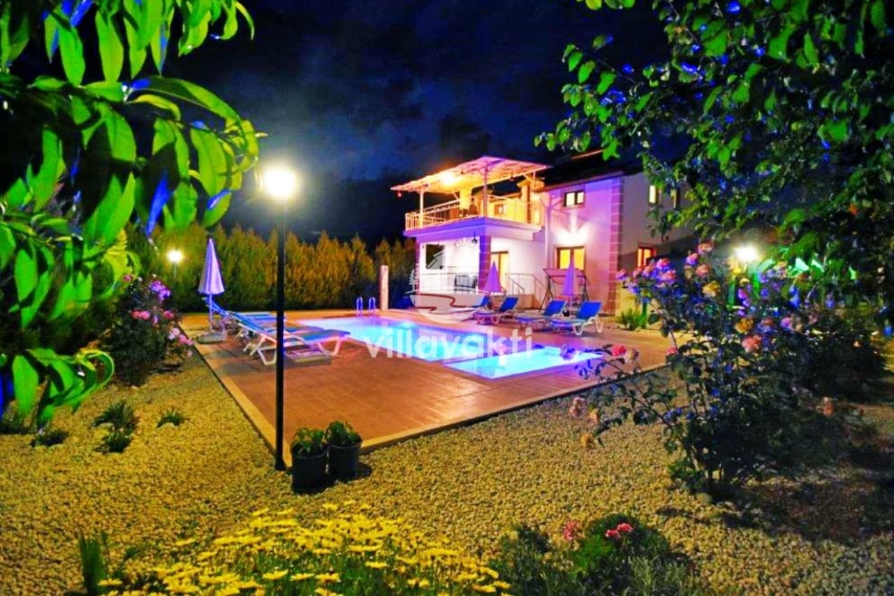 Aydınlatmalı havuz kenarı ve bahçesi olan iki katlı villa.