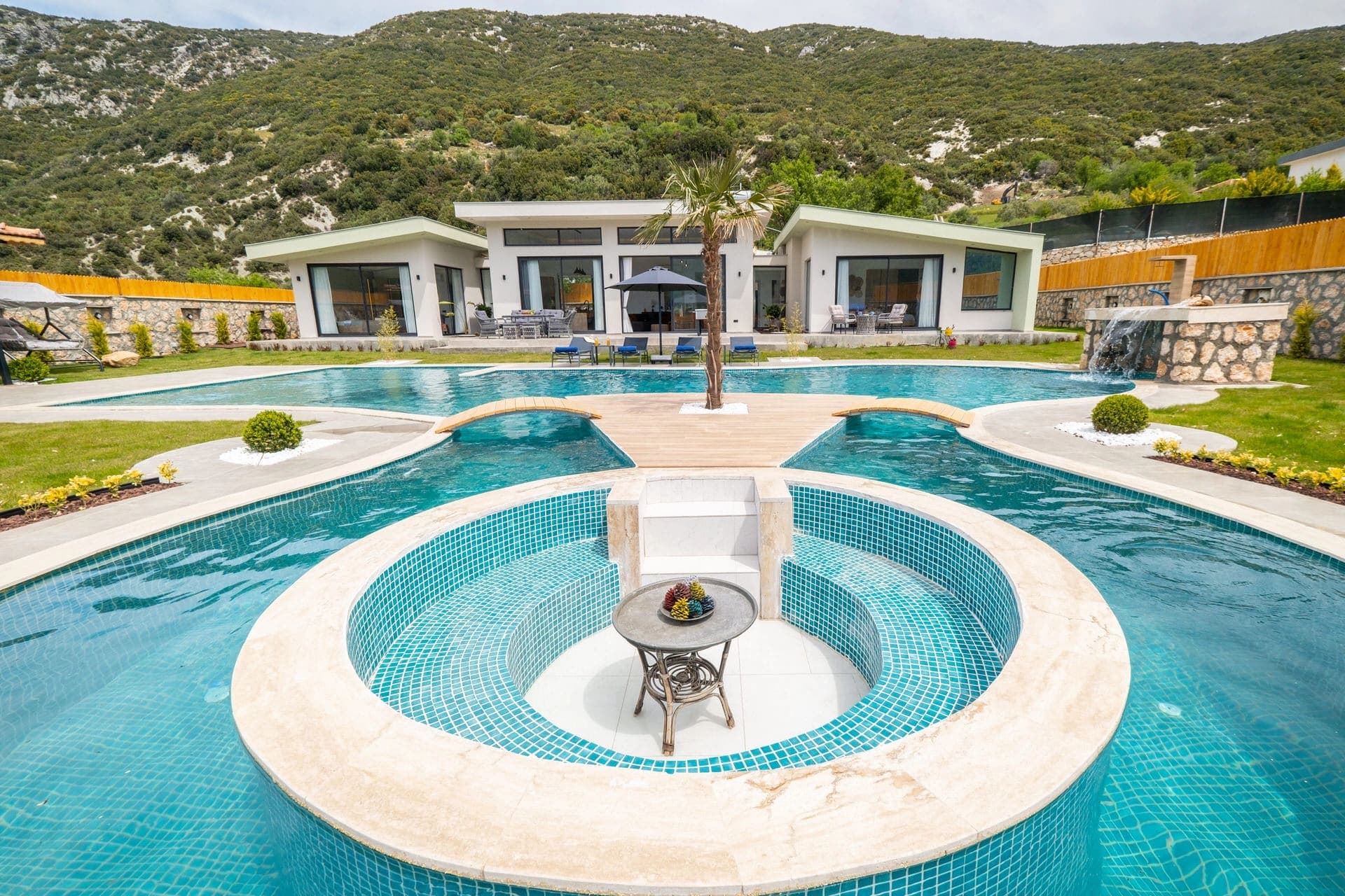 Önünde geniş havuz ve jakuzi bölümü olan dağ manzaralı villa.