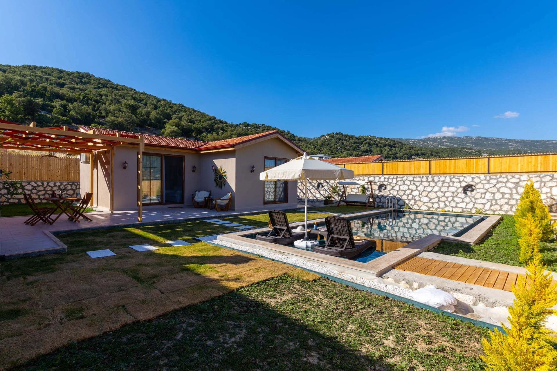 Bahçesinde havuz ve şezlonglar olan tek katlı villa.