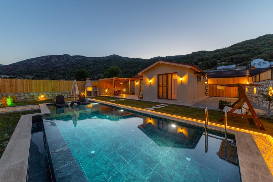 Akşam vaktinde havuzlu, bahçeli ve dağ manzaralı tek katlı müstakil villa.