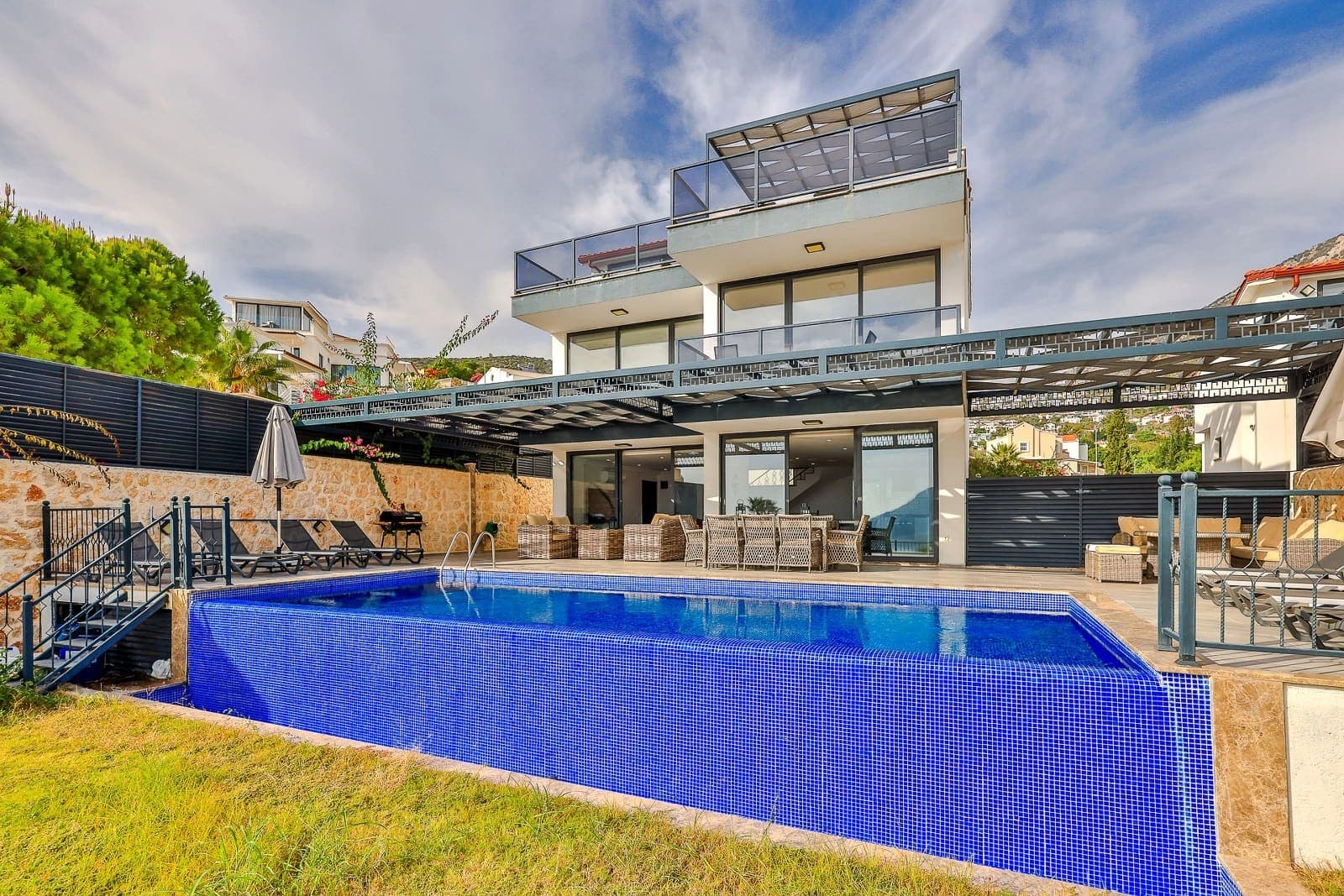 Önünde mavi havuz ve şezlonglar olan, iki katlı modern villa.