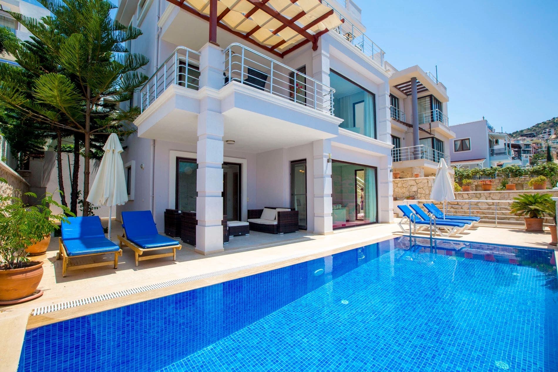 Mavi havuzun kenarında şezlonglar ve şemsiyeler bulunan çok katlı villa.
