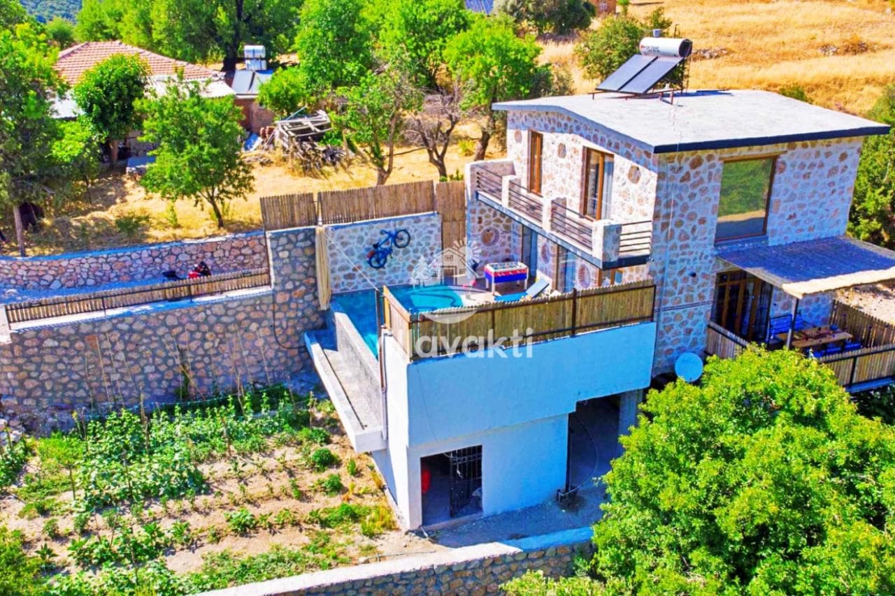 Taş duvarlı bahçesi ve havuzu olan taş kaplamalı iki katlı villa.