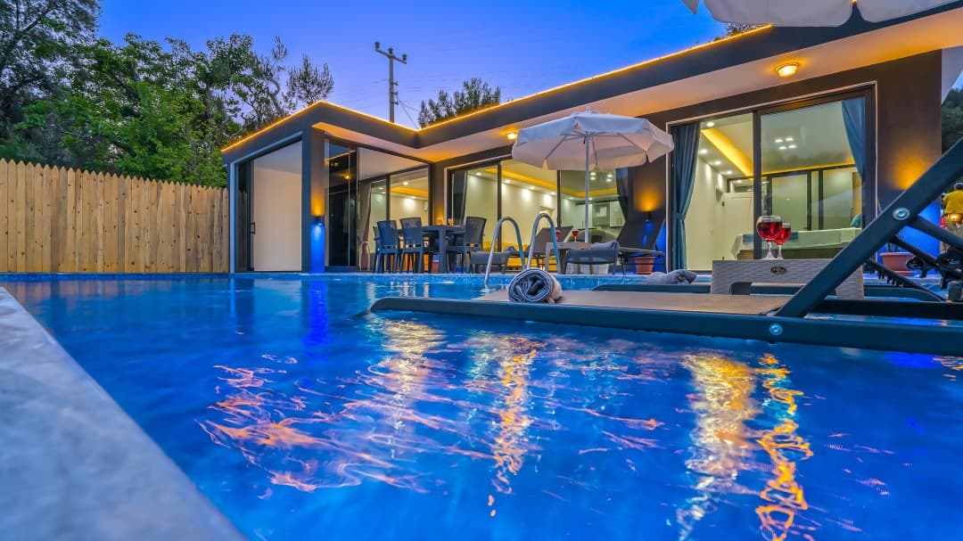 Akşam aydınlatmalı modern villanın önünde şezlonglu havuz.