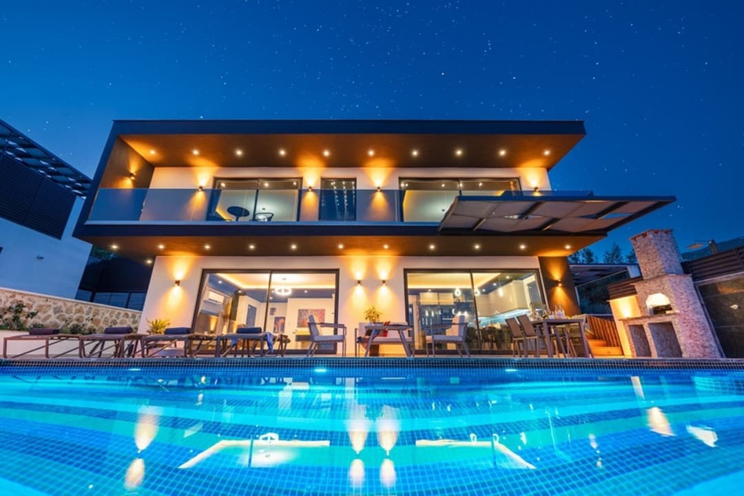 Gece aydınlatmalı, havuzlu ve yıldızlı gökyüzü altında iki katlı modern villa.