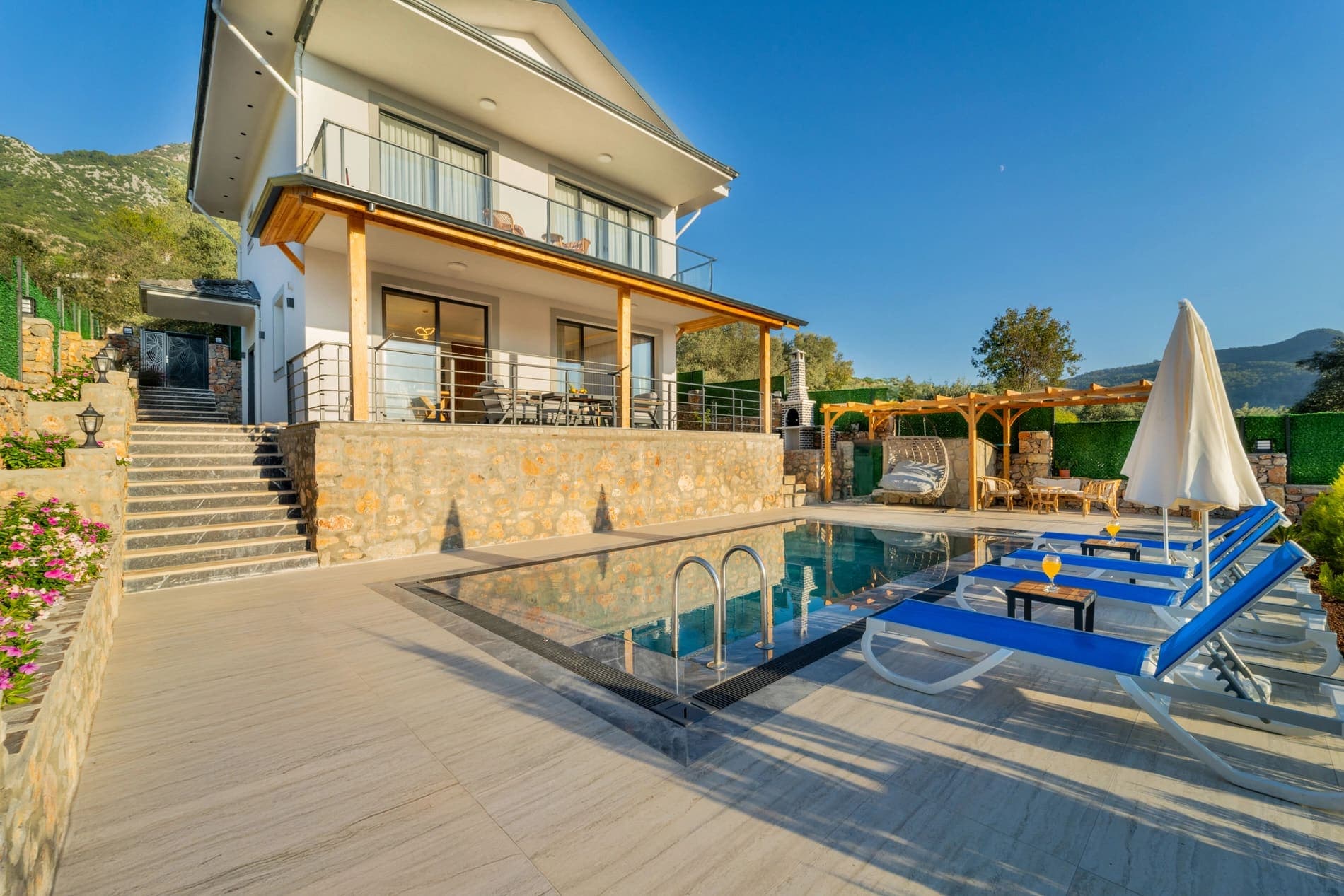 Önünde havuz ve şezlonglar bulunan iki katlı beyaz villa dış cephesi.