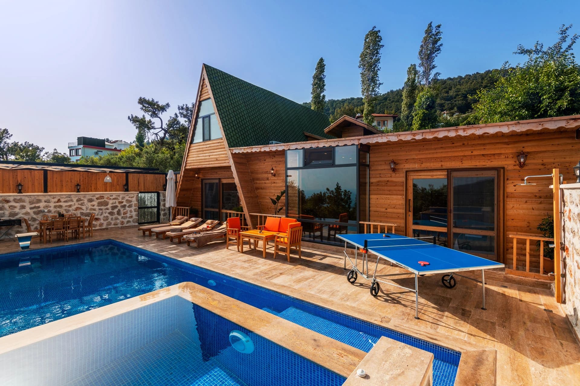 Ahşap cepheli bungalov tarzı villanın havuzu, şezlongları ve masa tenisi.