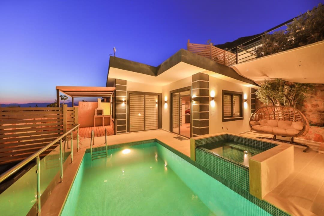 Akşam vakti aydınlatılmış havuzu, jakuzisi ve bahçesinde salıncak bulunan modern villa dış görünümü.