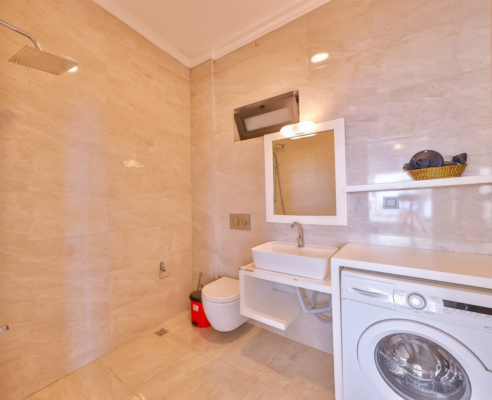 Bej seramik kaplı banyoda duş başlığı, lavabo ve çamaşır makinesi.