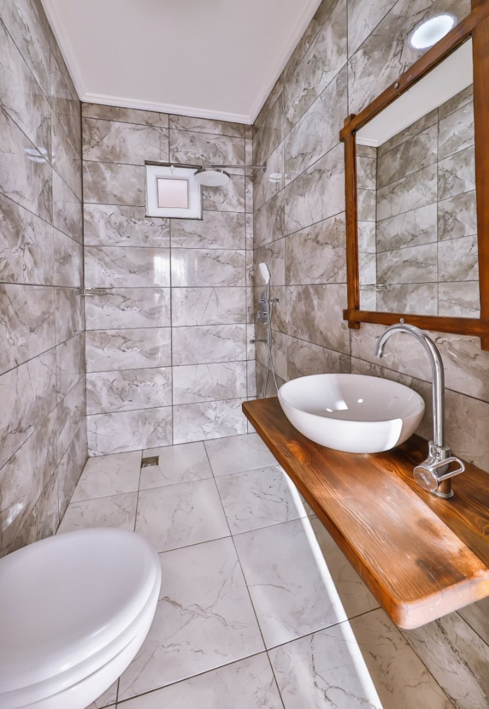 Mermer kaplı duş alanına sahip modern banyoda ahşap tezgâhlı lavabo.
