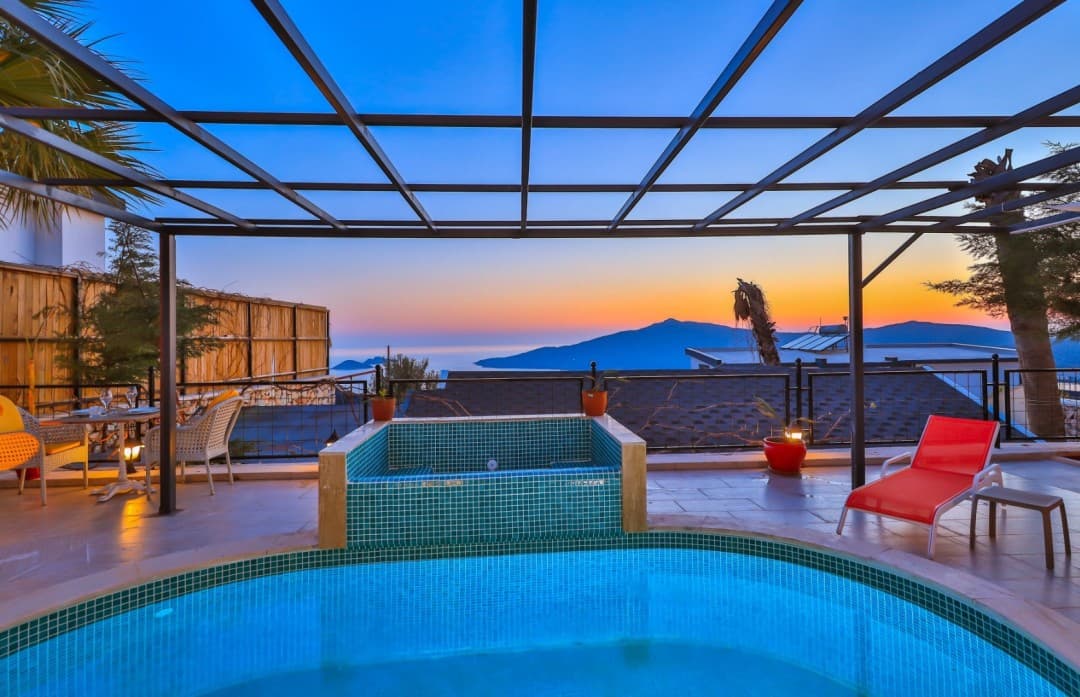 Gün batımında deniz ve dağ manzaralı, havuzlu ve şezlonglu villa terası.