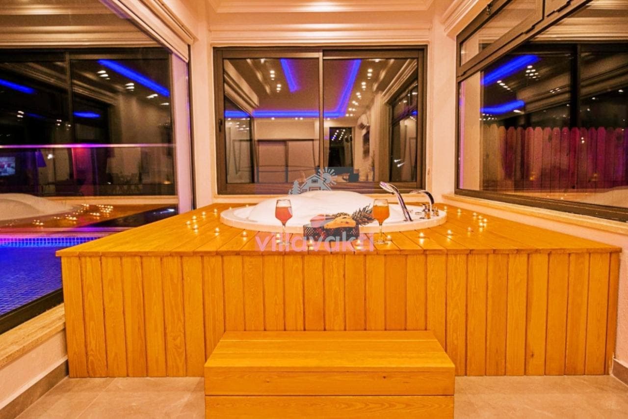 Ahşap kaplamalı platform üzerinde yuvarlak jakuzi, bardaklar ve mumlarla süslenmiş.