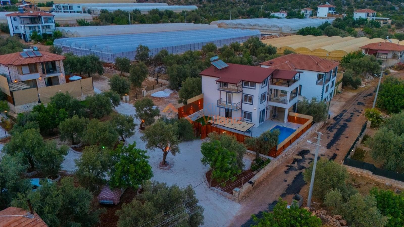 Ağaçlar arasında kalan, havuzlu ve kiremit çatılı müstakil villanın havadan görünümü.