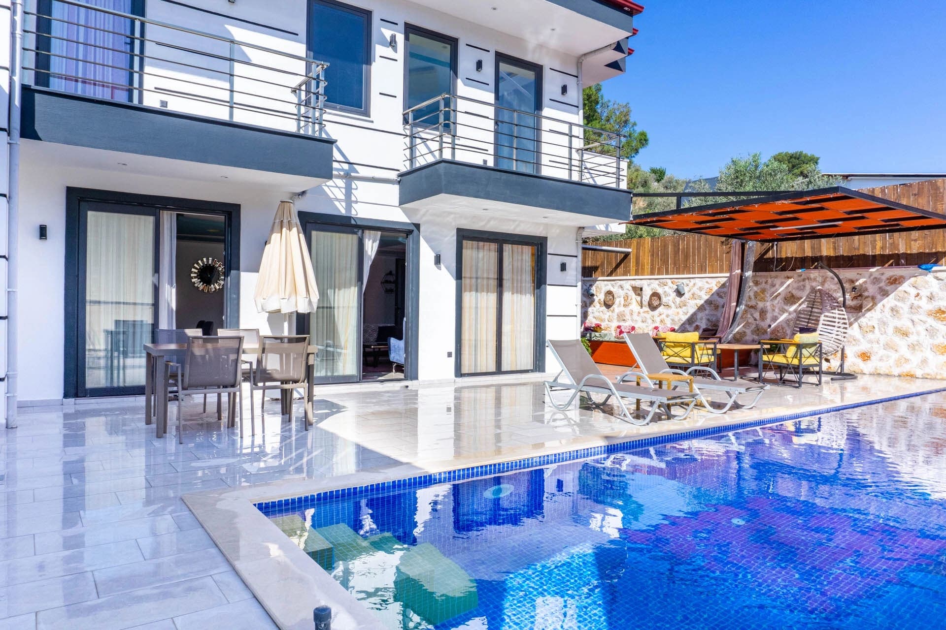 Mavi havuz kenarında şezlonglar ve arka planda beyaz dış cepheli iki katlı villa.