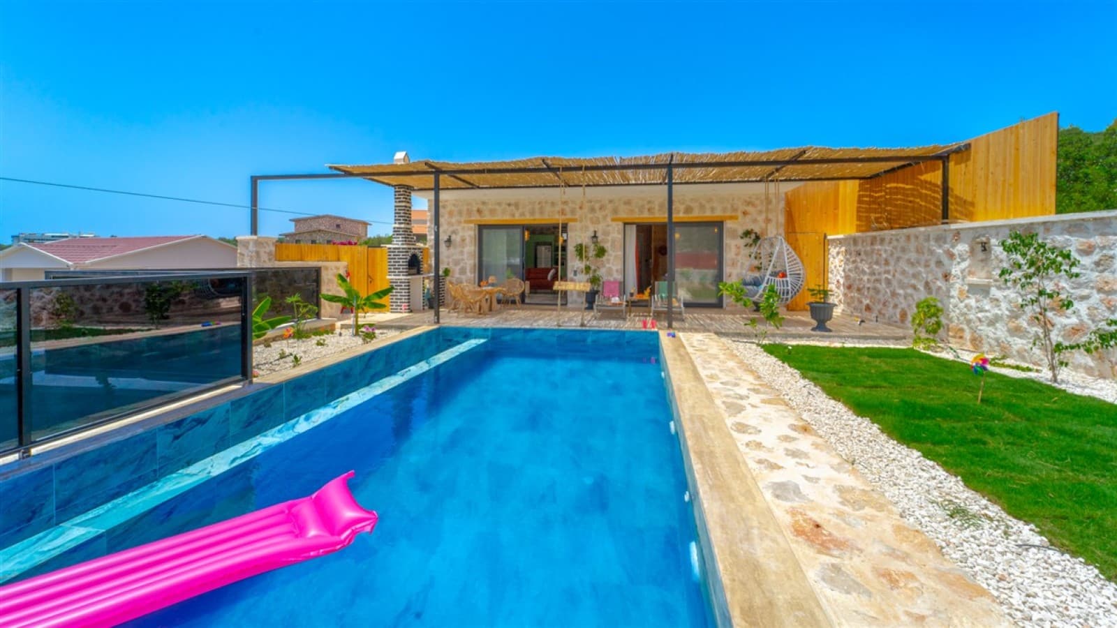 Mavi havuzunda pembe yatak bulunan, taş duvarlı ve çardaklı villa bahçesi.