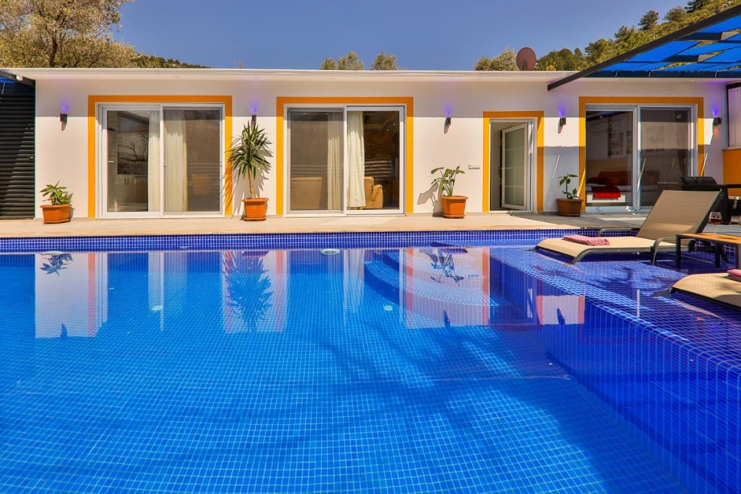 Mavi mozaik kaplı havuzun arkasında beyaz dış cepheli villa.