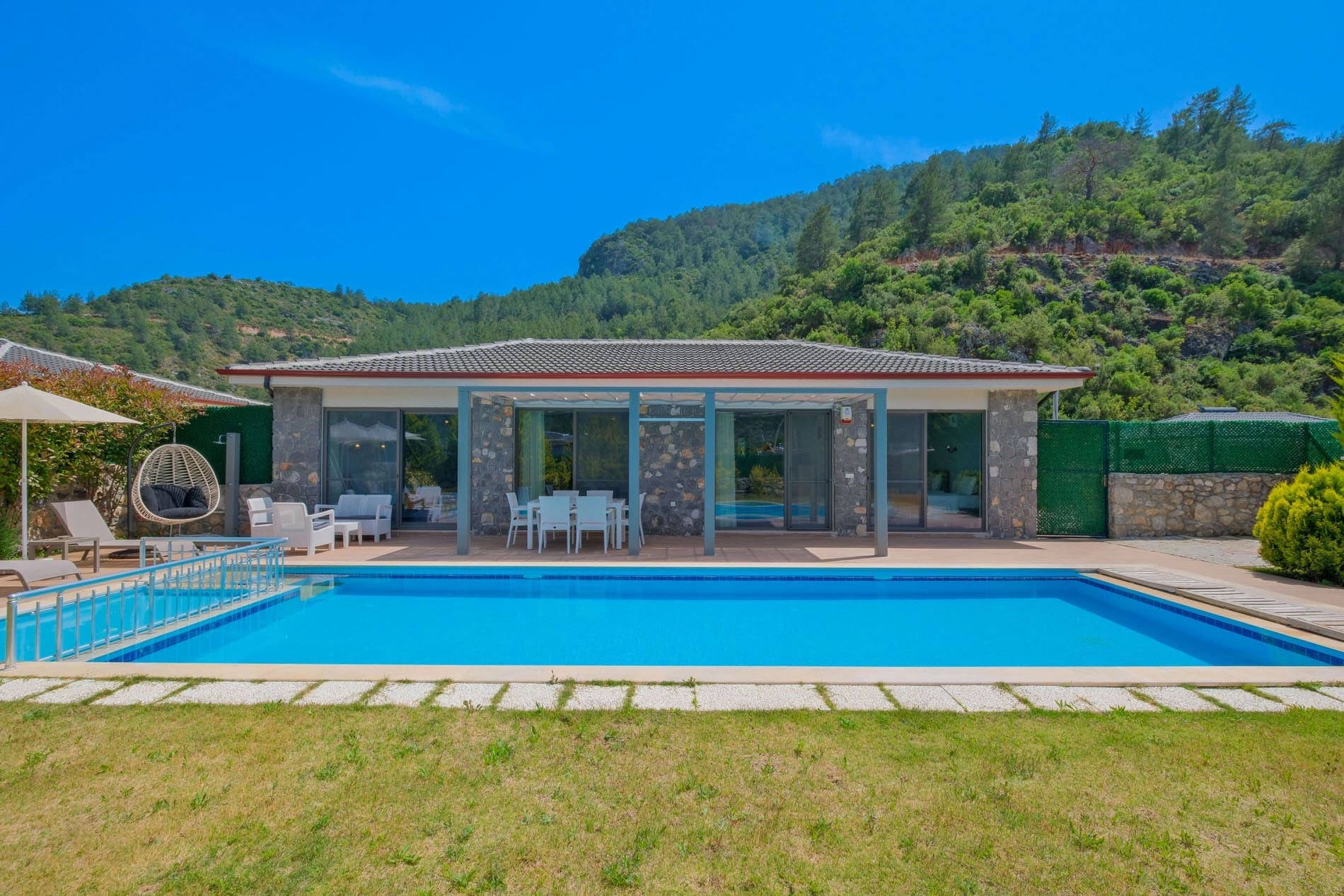 Önünde yüzme havuzu ve çim alan bulunan tek katlı taş villa.