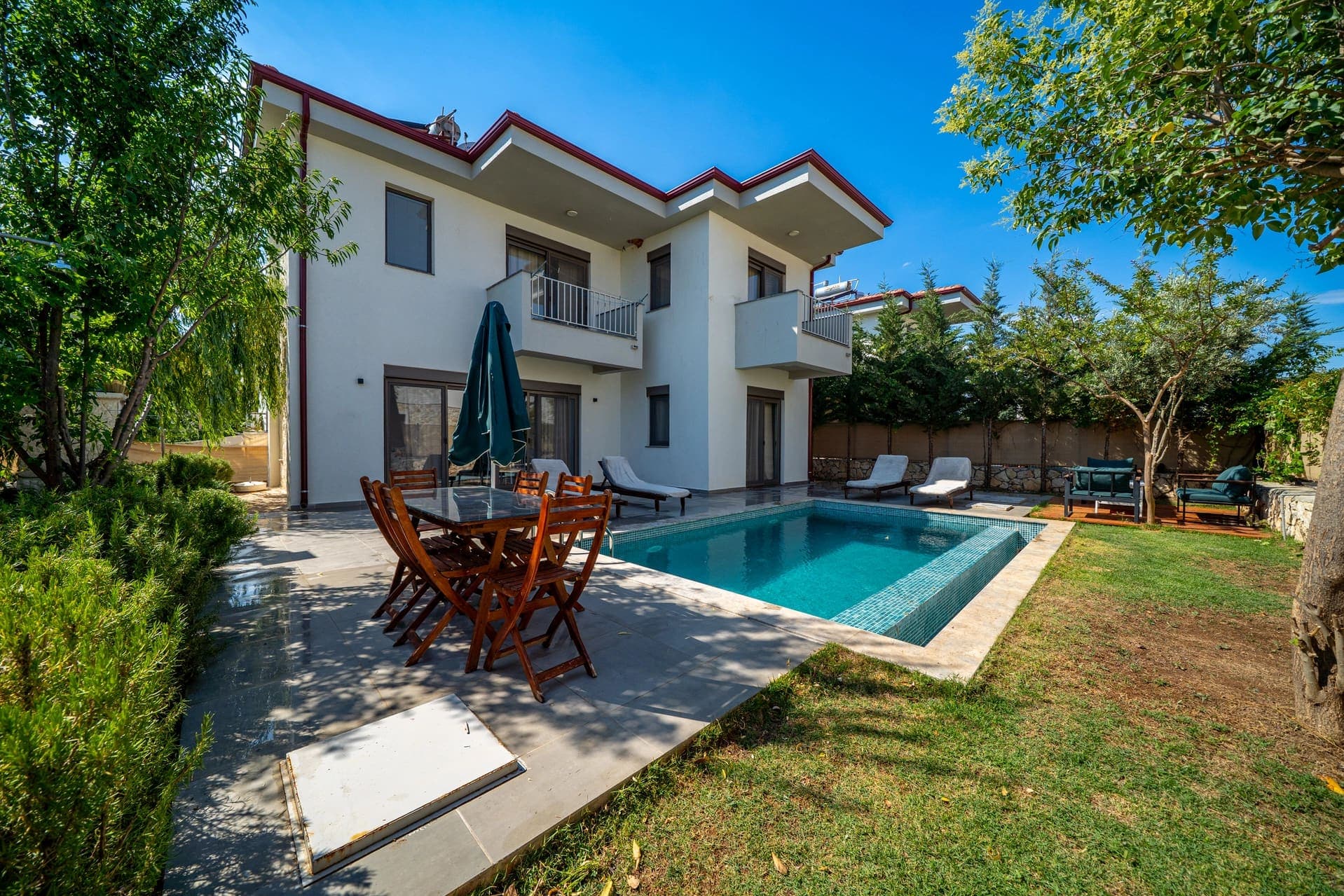 Yeşillikler içindeki bahçede özel yüzme havuzu ve şezlonglar bulunan iki katlı villa.