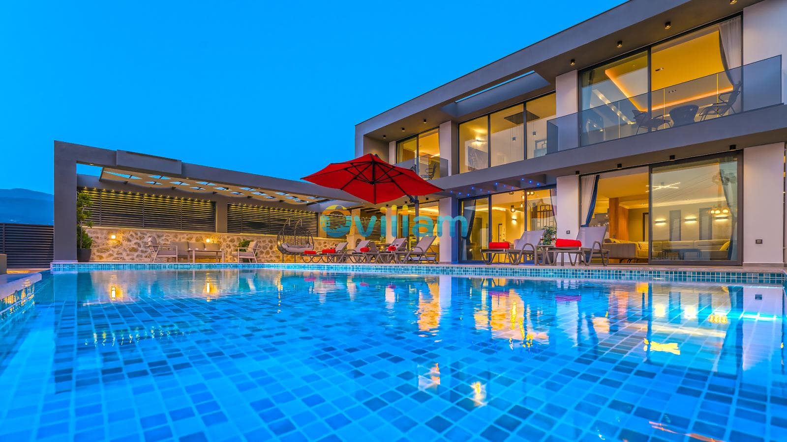 Akşam ışıklandırmalı havuz ve şezlongların bulunduğu iki katlı modern villanın dış cephesi.