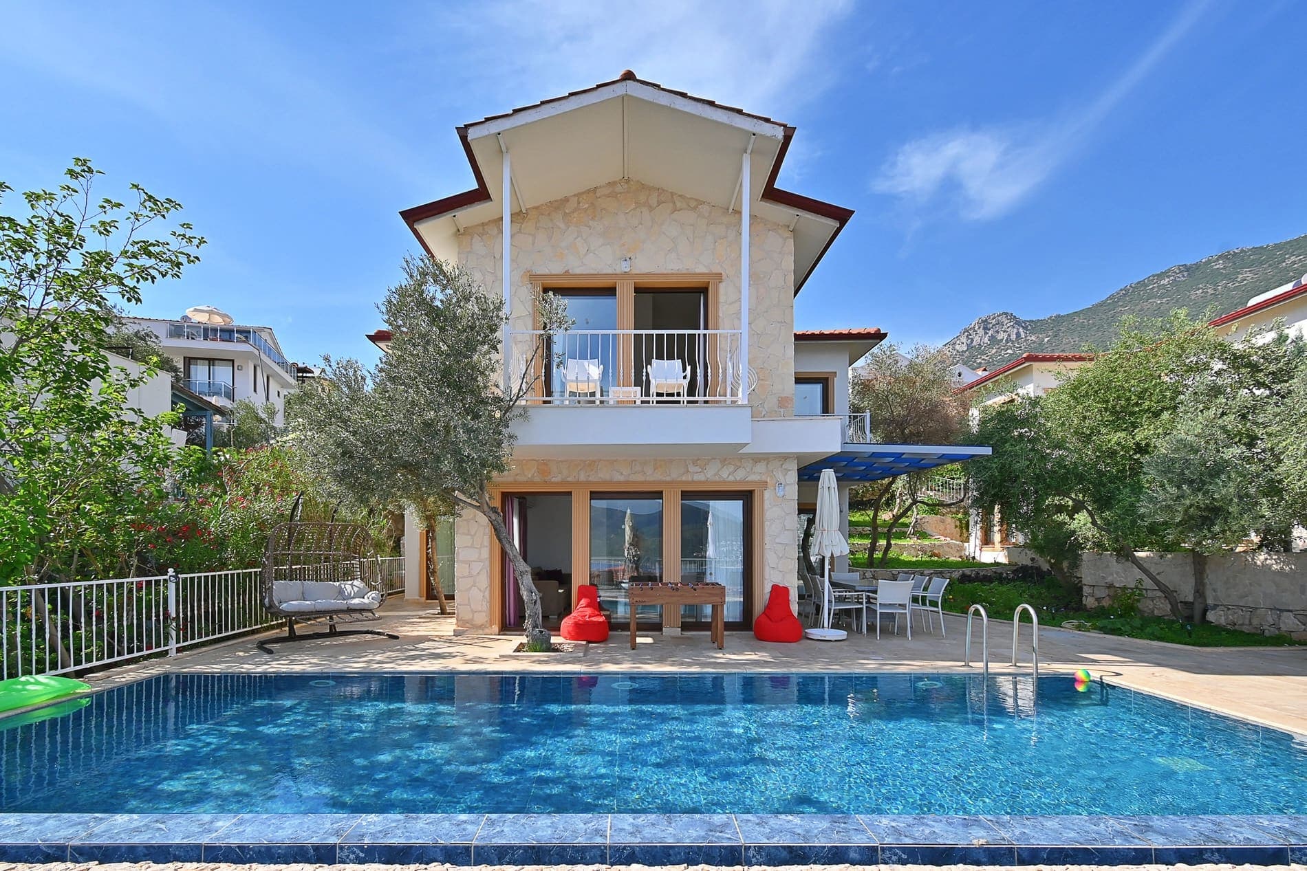 Taş cepheli, balkonlu iki katlı villanın önünde havuz ve bahçe alanı.
