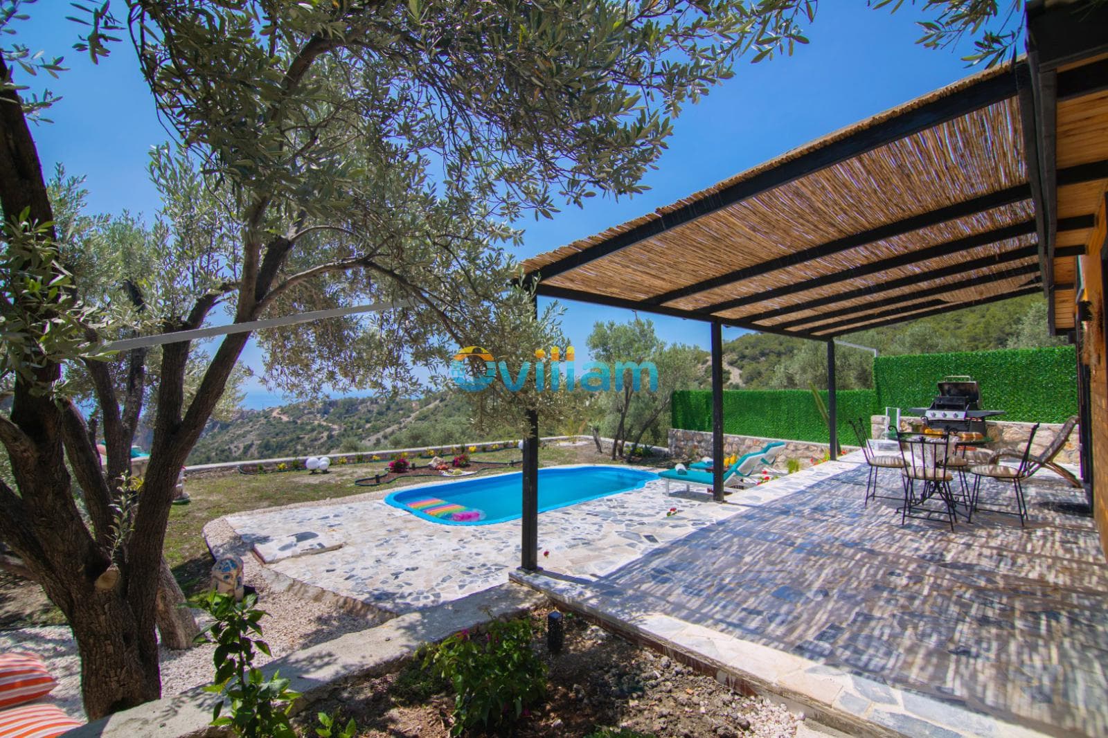 Ağaç gölgeli terası ve ahşap pergolası olan havuzlu villa bahçesi.