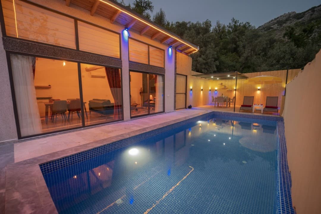 Akşam ışıklandırmalı havuzu ve geniş camlı oturma alanı olan villa.