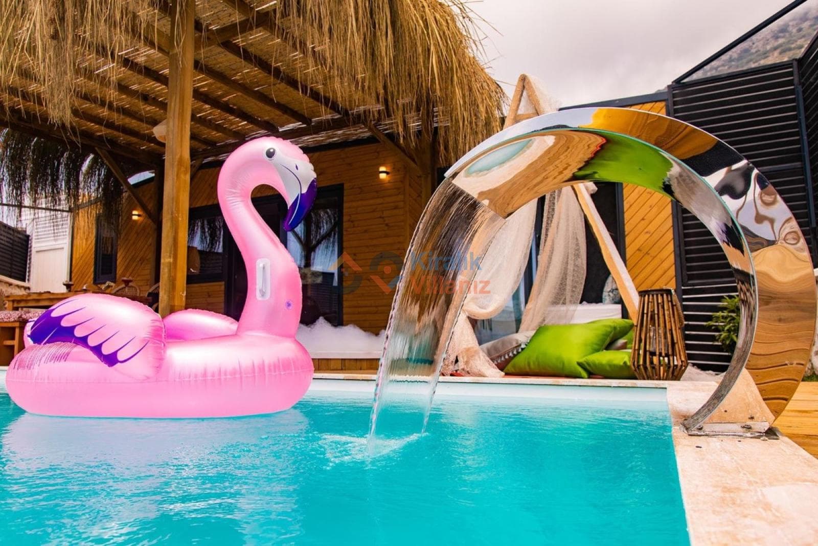 Ahşap pergolalı havuz kenarında pembe flamingo deniz yatağı ve şelale detaylı havuz.