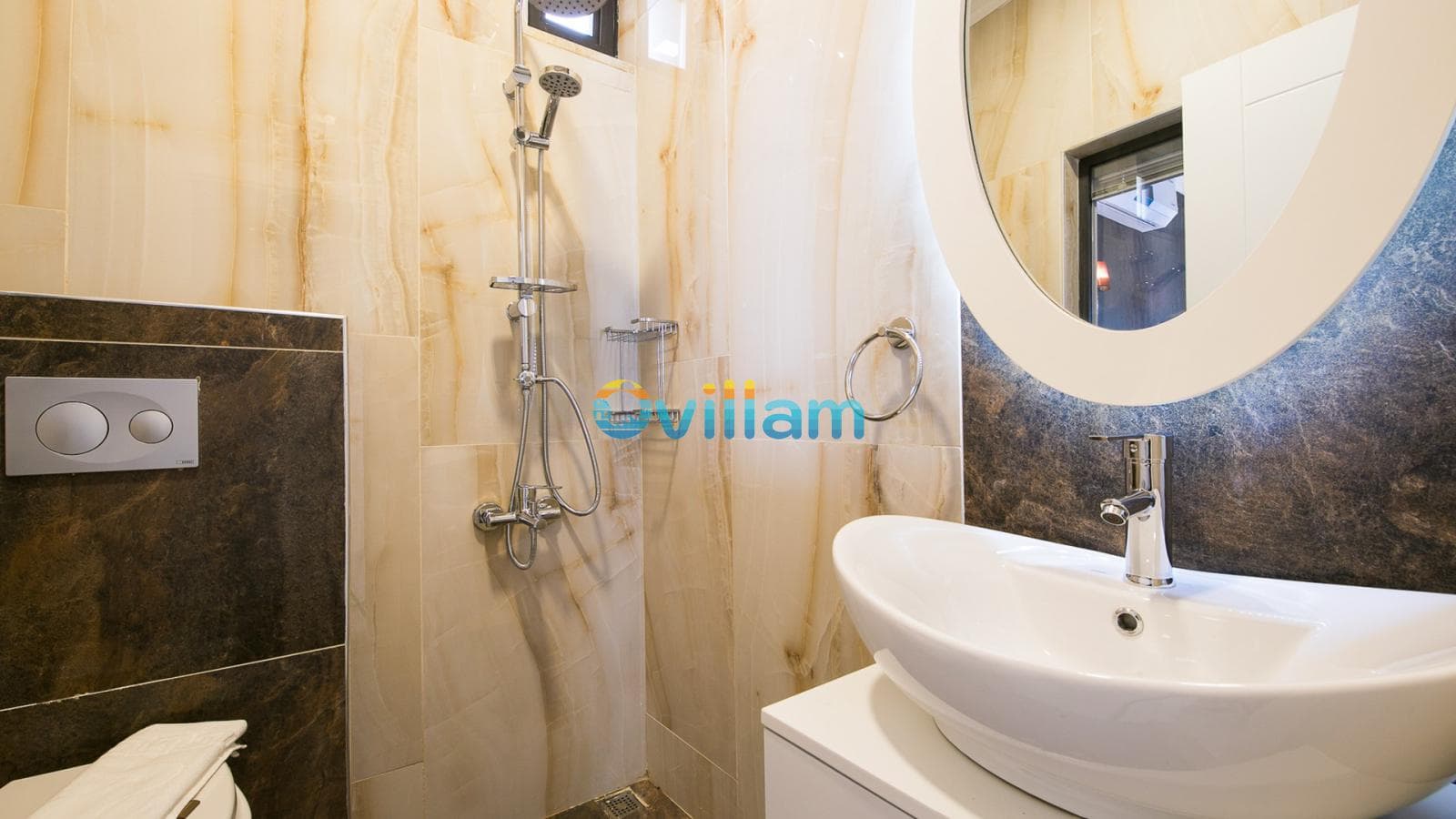 Mermer duvarlı duşakabin alanı, lavabo ve yuvarlak ayna bulunan banyo.