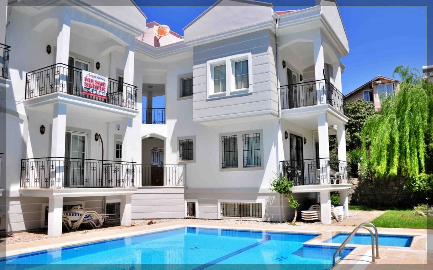 Önünde yüzme havuzu bulunan, siyah korkuluklu balkonlara sahip beyaz dış cepheli villa.